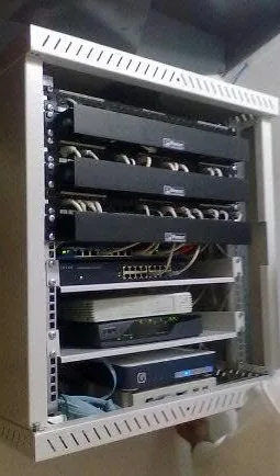 Επίτοιχο rack με τρία patch panel μπαλωμένα με λευκά καλώδια, έναν μεταγωγέα από κάτω και δύο συσκευές στα χαμηλότερα επίπεδα.